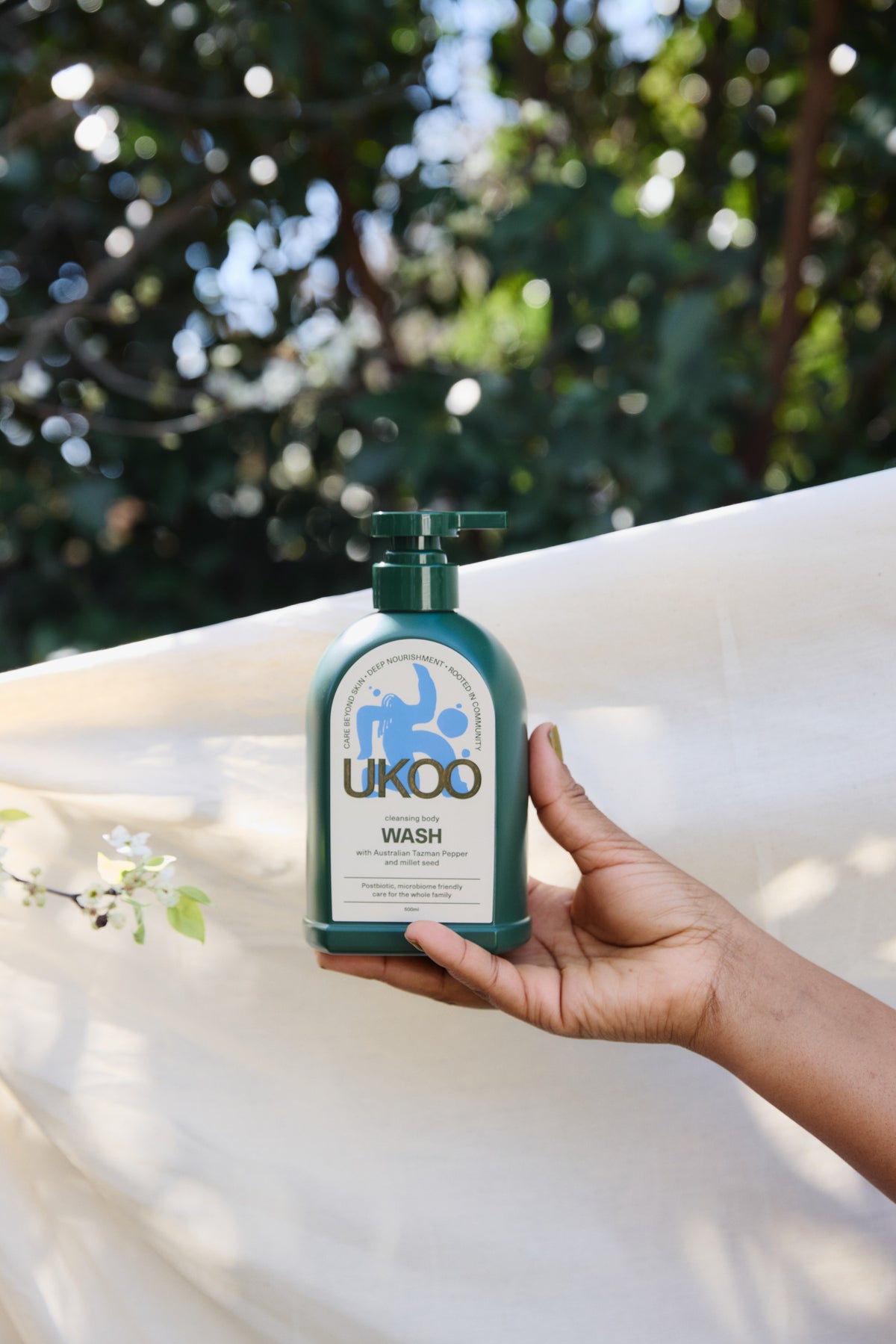 A hand holding UKOO Cleansing Body Wash in sunlight against greenery
