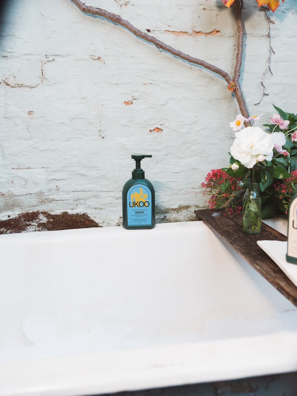 UKOO fragrance-free body wash on the edge of an old bathtub beside garden flowers